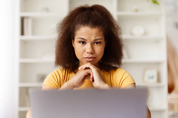 istock Serious black woman thinking deeply while looking at laptop screen at home 2224271143