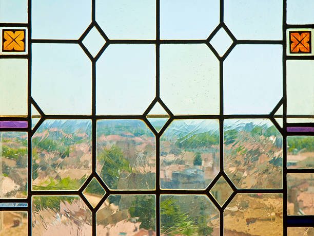 VINTAGE STAINED GLASS WINDOW WITH GEOMETRIC PATTERN and textured panes, offering a blurred view of rooftops and trees in daylight, made with handmade glass set in lead came strips
