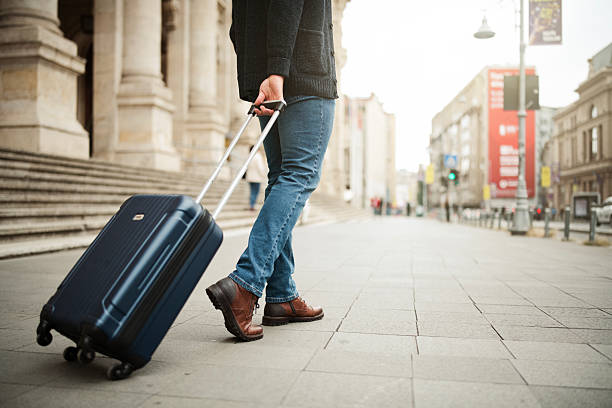 Lower section of a businessman on a work trip holding a suitcase in a city.