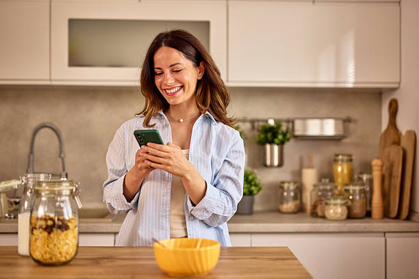 istock Young Woman Using Smartphone and Smiling in Kitchen 2224274687