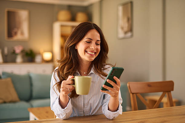 istock Smiling woman drinking coffee and using smartphone at home 2224274898