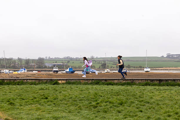 A wide angle view of a brother and sister chasing each other along a stone wall whilst on a family day trip to Alnmouth on the coast in Northumberland. They are wrapped up for the overcast weather and enjoying some family time together.