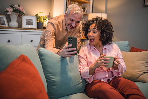 istock A black woman sits on a sofa drinking coffee while her husband shows her something on his mobile phone, which makes them have a lot of fun 2224277727