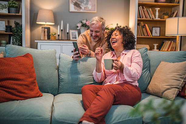 istock A black woman sits on a sofa drinking tea while her husband shows her something on his mobile phone, which makes them have a lot of fun 2224277833