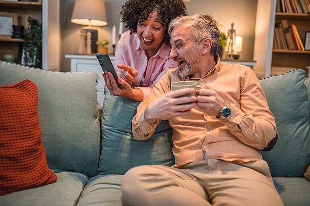 istock Smiling multiracial woman showing her husband something on her mobile phone while sitting on the sofa in the living room 2224282702