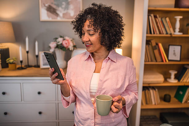 istock Smiling senior black woman using mobile phone to surf internet with coffee 2224282862