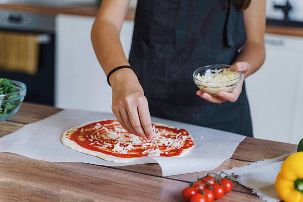 istock Girl adding grated cheese on pizza base 2224284212