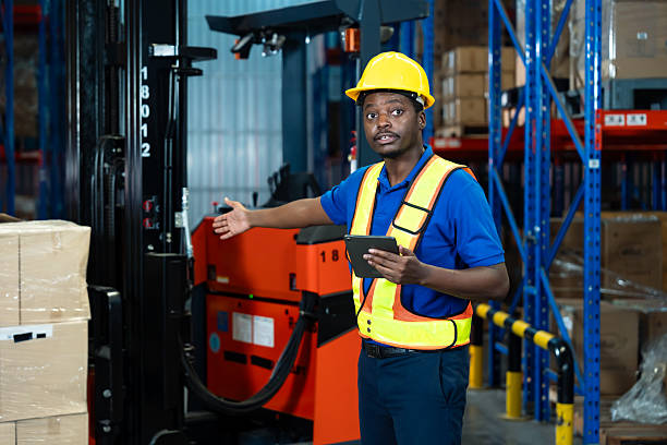 istock African male adult warehouse employee explaining logistics task using digital tablet standing in industrial storage area wearing safety helmet and vest focusing on inventory coordination 2224284264