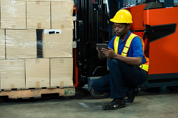 istock African male inventory worker sitting near wrapped boxes using digital tablet to manage warehouse stock beside forklift in industrial storage building, inside logistics warehouse. 2224284299