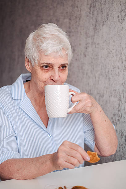 istock An elderly woman in a blue blouse drinks tea with cookies while sitting in the kitchen. 2224284537