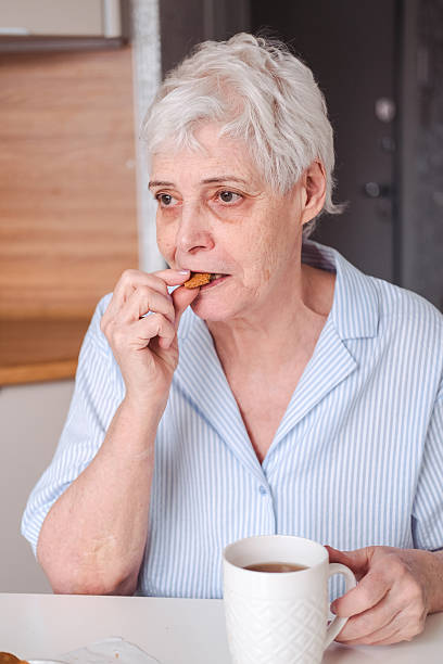 istock An elderly woman in a blue blouse drinks tea with cookies while sitting in the kitchen. 2224284547