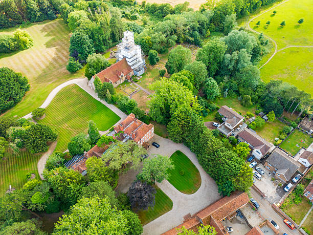 Aerial view of a larger Manor House and lush lawns seen near an old English church with the spire under renovation as can be seen with the scaffolding in place. stock photo