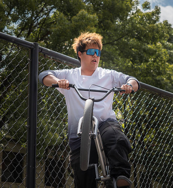 Action-packed moment capturing a BMX rider executing an impressive jump over a chain-link fence, set against a backdrop of lush greenery and partly cloudy skies. The dynamic scene conveys excitement and skill, suitable for sports, extreme sports, or action-themed content.