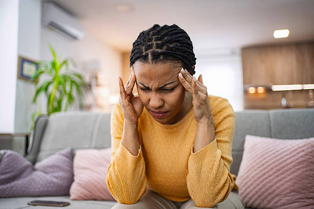 istock Young woman suffering from a headache, touching her temples while sitting on the sofa 2224292122
