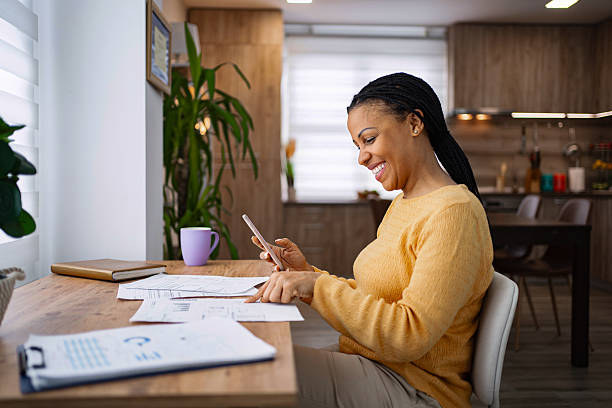 istock Smiling black woman using smartphone and analyzing reports at home 2224292289