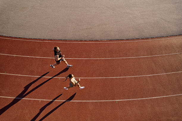 Two athletes running on track from above with long shadows