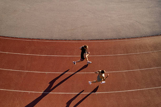 istock Two athletes running on track from above with long shadows 2224298125