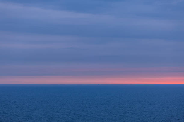 View from a cruise ship in the Norwegian Sea at sunset: the endless horizon glows with soft pink and blue tones. A tranquil ocean and sky background perfect for serene visuals.