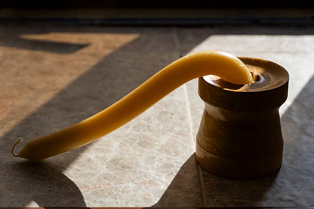Yellow candle melted and bent under scorching heat in a wooden holder on tiled surface. Sunlight and shadows emphasize the intense heat