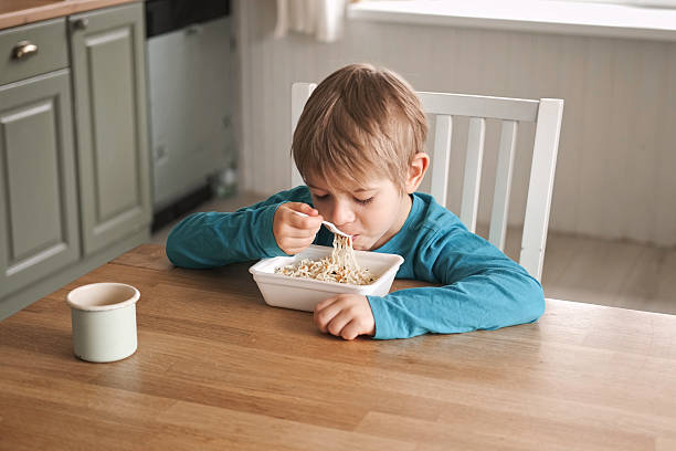 istock 6 years old boy eats instant noodle from box. Child is eating spaghetti. Lunch time. A good appetite. Tasty children food. Close-up portrait. Carbs dinner. Fast food. Kid eating by himself with fork. 2224305757