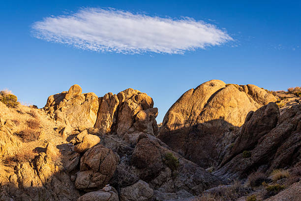 Impressive rock formations bathed in golden light under a vast blue sky in Alabama Hills, California, create a breathtaking natural landscape