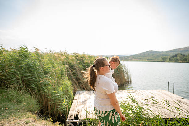 Mother holding baby girl over lake and nature background. Autumn season. Motherhood.