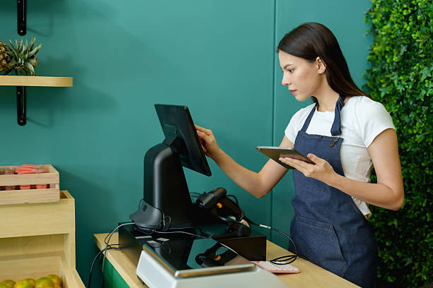 istock Caucasian female owner in apron using tablet configuring POS system at counter preparing to open small fruit business inside modern grocery store during morning shift 2224310857