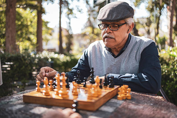 Senior adult man concentrating on a chess game in a sunny park setting, highlighting strategic thinking and leisure activity in a natural environment