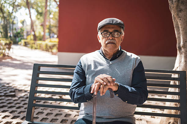 istock Senior hispanic man sitting on bench in park holding cane 2224311499