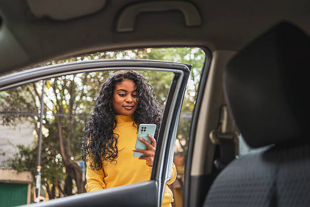 istock Young woman using smartphone by car door 2224311569
