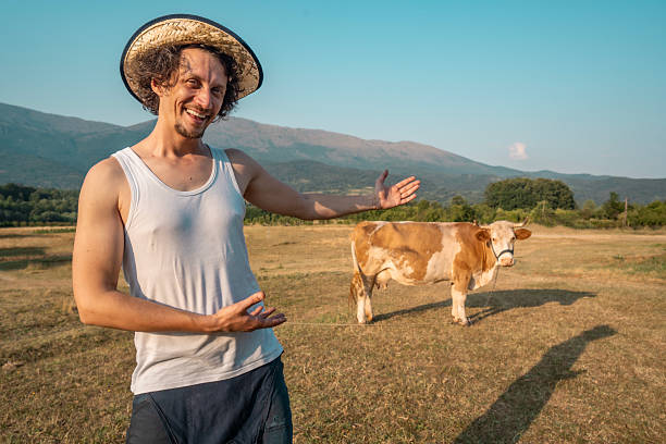 A cheerful man in casual clothing poses with a cow in a picturesque rural landscape on a sunny day, embodying countryside charm, warmth, and a connection to nature and agriculture.