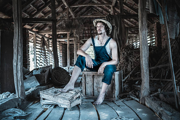 Farmer resting in a rustic wooden barn surrounded by hay, old wooden crates, and natural light. Evokes a sense of simplicity, rural life, and reflection within an authentic countryside setting.