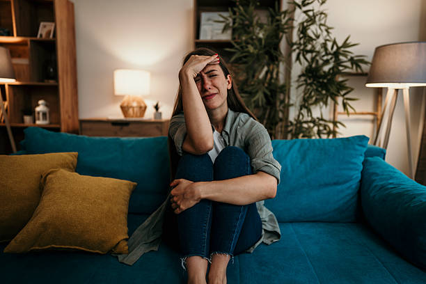 istock Sad young woman sitting on sofa holding head and crying 2224331673