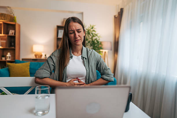 istock Young woman suffering from stomach ache while working from home 2224332004