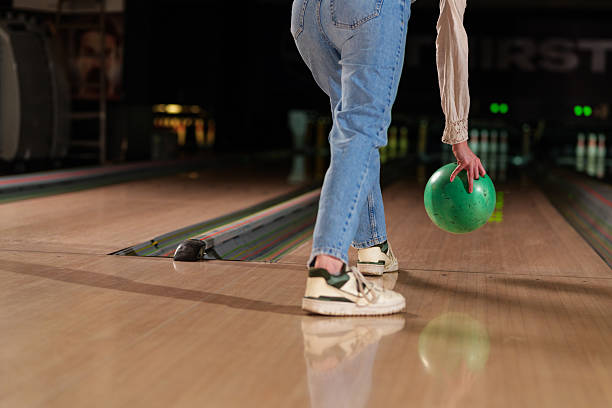 istock Young woman playing bowling holding a green ball and getting ready to throw it, low angle view of legs, jeans and sneakers 2224335586