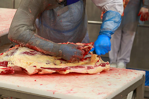 A meat market stall where a butcher's hand is cutting hanging lamb meat.