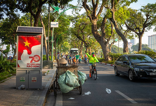 A female cyclist waves as she cycles past a street cleaner on Thanh Nien Road on a Sunday morning in Hanoi, Vietnam.