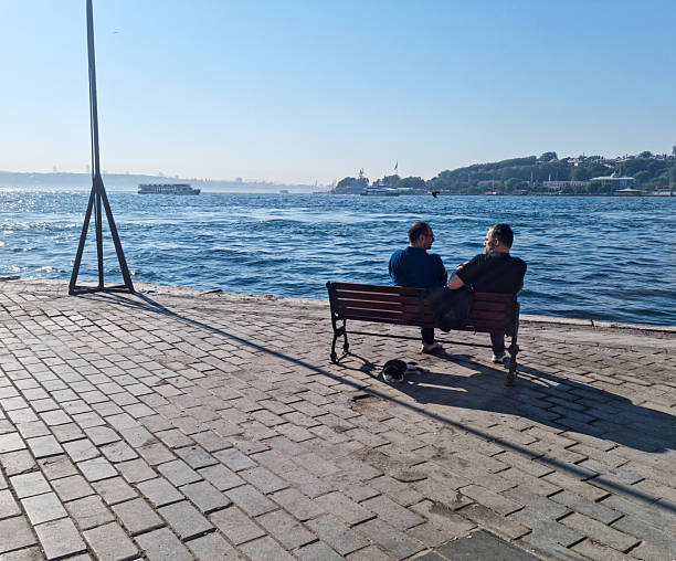 Two men sitting on the bench on the beach, chatting and enjoying
