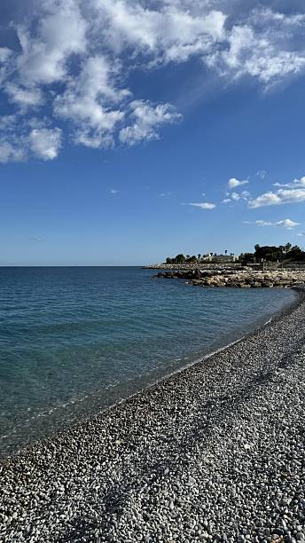 istock Serene coastal view with pebbles and clear blue water under a bright sky 2224343056