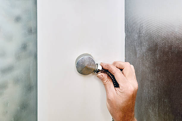 istock Plumber inside shower cabin tightens hose nut at connection point, fixing leak in modern enclosed shower space. 2224346238