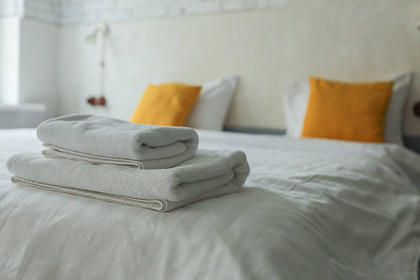 istock Folded white towels on a neatly made bed with white linens and yellow pillows in a bright modern bedroom with a cozy atmosphere 2224384253