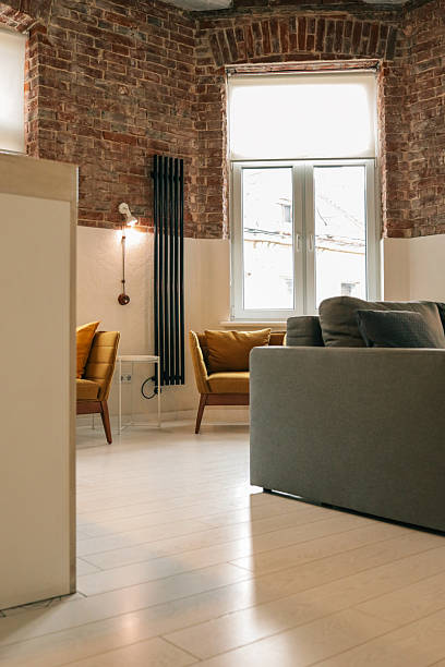 istock Bright loft-style living space with mustard armchairs, white table, gray sofa, exposed red brick walls, and large window providing natural light 2224393975