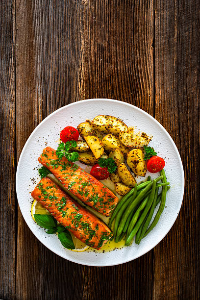 Seared salmon steaks with green string beans and roasted potatoes on wooden table