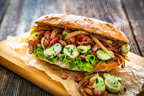 Takeaway sandwich with broad beans, fried bacon and caramelized onion on wooden table