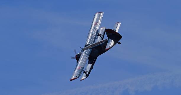 A dynamic shot of an Antonov An-2 biplane in Soviet livery performing a banking turn against a clear blue sky, seen from above or high angle.