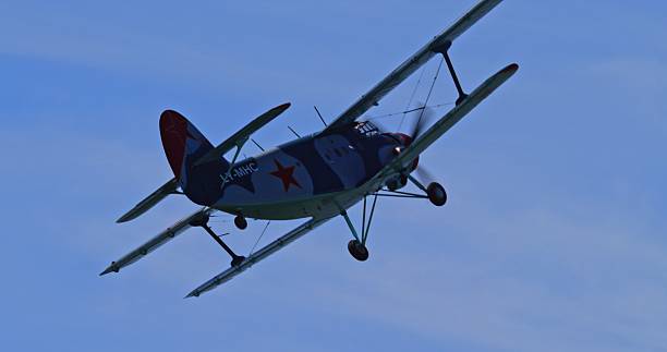 A sharp, close-up view of an Antonov An-2 biplane flying against a clear blue sky, clearly showing its LY-MHC registration and red star insignia.