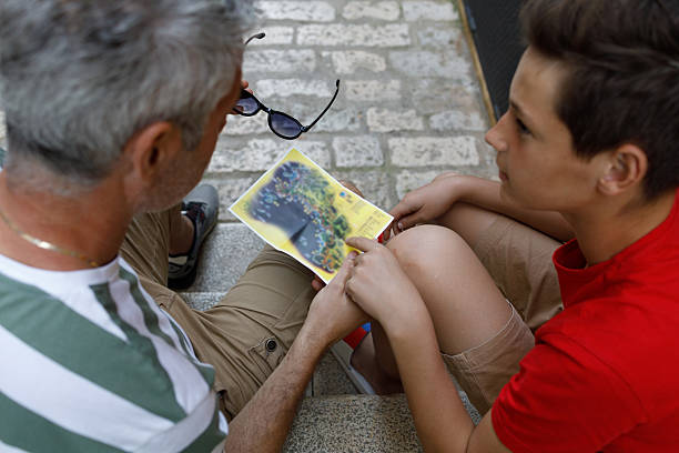 Young boy hiking in grassy field, attentively studying map and compass outdoors. With backpack on shoulders, tourist focused on navigating or planning his route in the mountains.