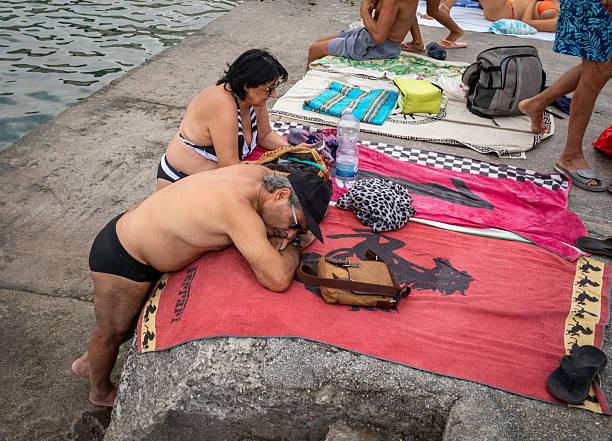 Miami Beach. USA. April.15.2025. Homeless man resting on sandy Atlantic Ocean beach with bags and clothes.
