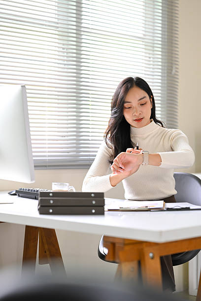 Businesswoman checking time on smartwatch, managing schedule in a bright office.