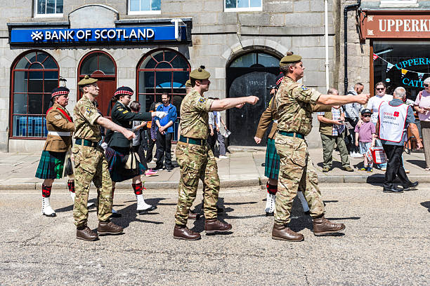 3rd July 2022: Scottish Game Fair. Rear view of a Highland Pipe Band playing at a traditional Scottish Game Fair in Perth. The pipe band have bagpipers and drummers. They are wearing traditional Highland dress, with kilts, sporrans and a traditional Scottish knife called a Sgian Dubh, tucked in their green wool socks.
